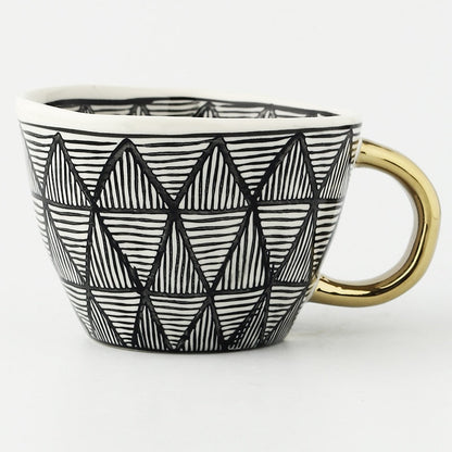 Tasse mit abstraktem geometrischem Muster und goldenem Henkel