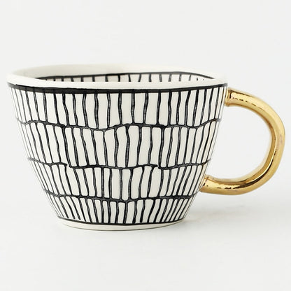 Tasse mit abstraktem geometrischem Muster und goldenem Henkel